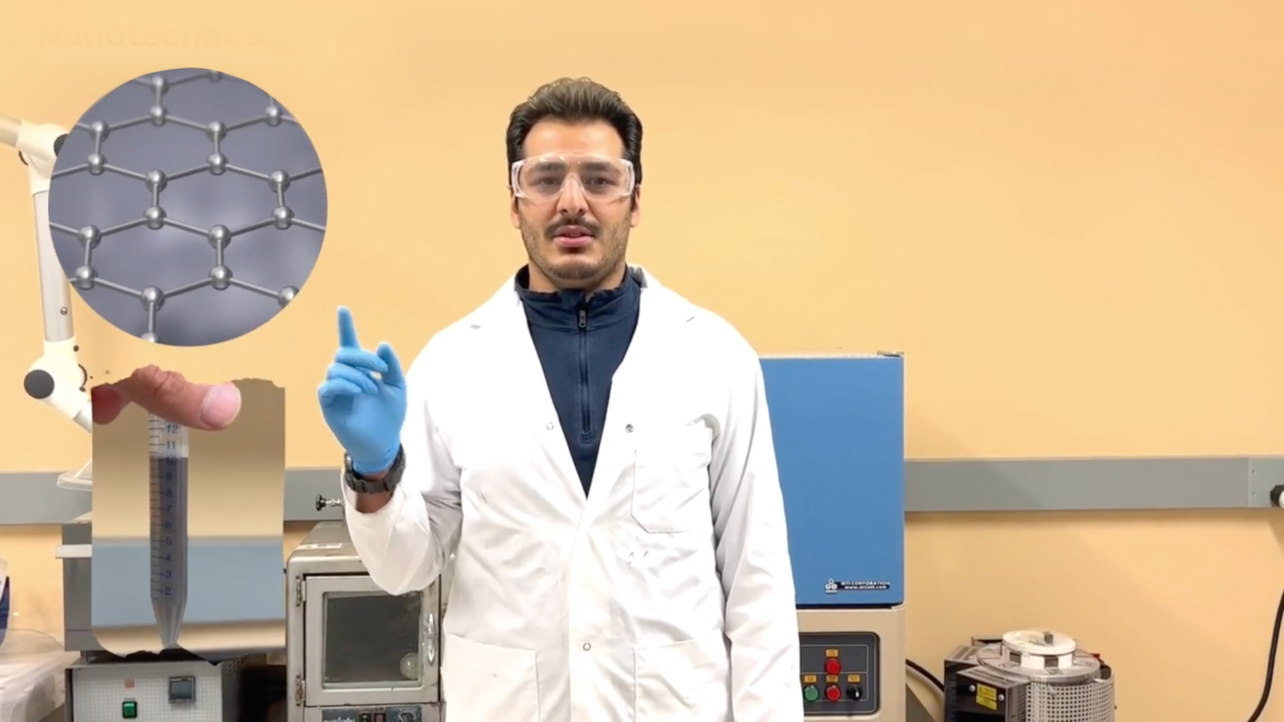 Scientifique portant des lunettes de protection étanches et un sarrau, dans un laboratoire, qui pointe une main gantée de bleu vers une bulle qui contient une image représentant la nanotechnologie.